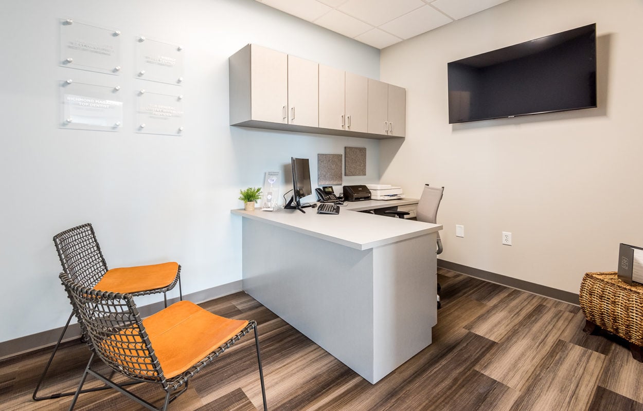 Contemporary dental consultation room with desk, seating area, cabinetry, and wood-look flooring